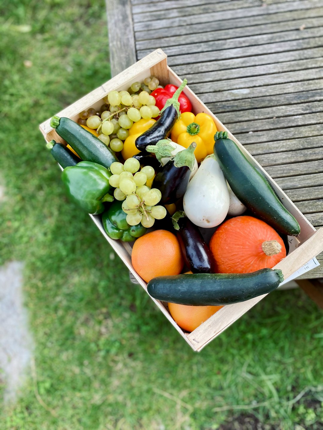 Wooden crate overflowing with colorful fruits and vegetables on a picnic table.